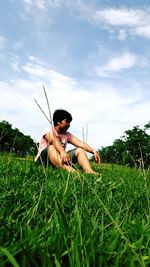 Woman sitting on grassy field against cloudy sky