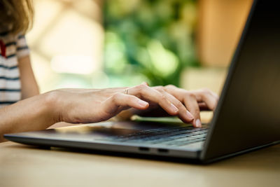 Hands typing on laptop keyboard. close up shot of woman using laptop in cafe