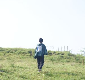 Rear view of man walking on field against clear sky