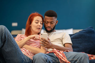 Young millennial diverse couple man and woman resting at home with mobile phone