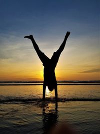 Silhouette man with arms raised on beach against sky during sunset