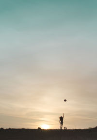 Silhouette man playing with ball against sky during sunset