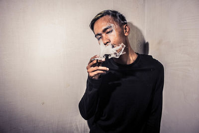 Portrait of man smoking cigarette against wall