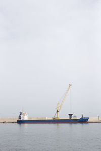 Ship by crane at harbor against sky