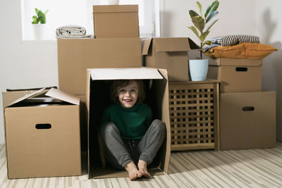 Cute toddler boy playing in cardboard box at new home.