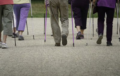 Low section of people holding nordic walking poles while walking on road