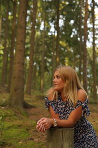 Thoughtful young woman looking away while standing by tree stump in forest