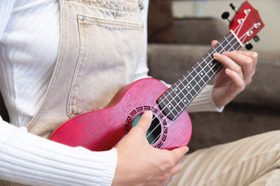 Close-up, a woman or girl plays the ukulele while sitting at home, on the floor. distance learning