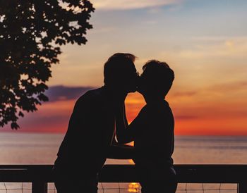 Silhouette couple kissing against sea during sunset