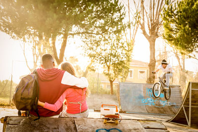 Rear view of young couple sitting at skateboard park during sunset