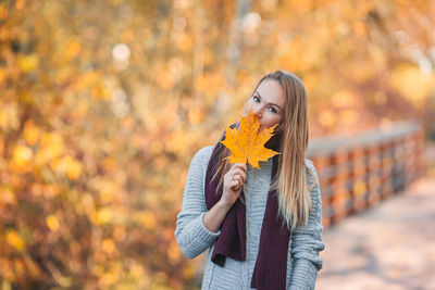 Close-up of woman holding autumn leaf against tree