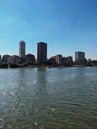 Sea by buildings against blue sky