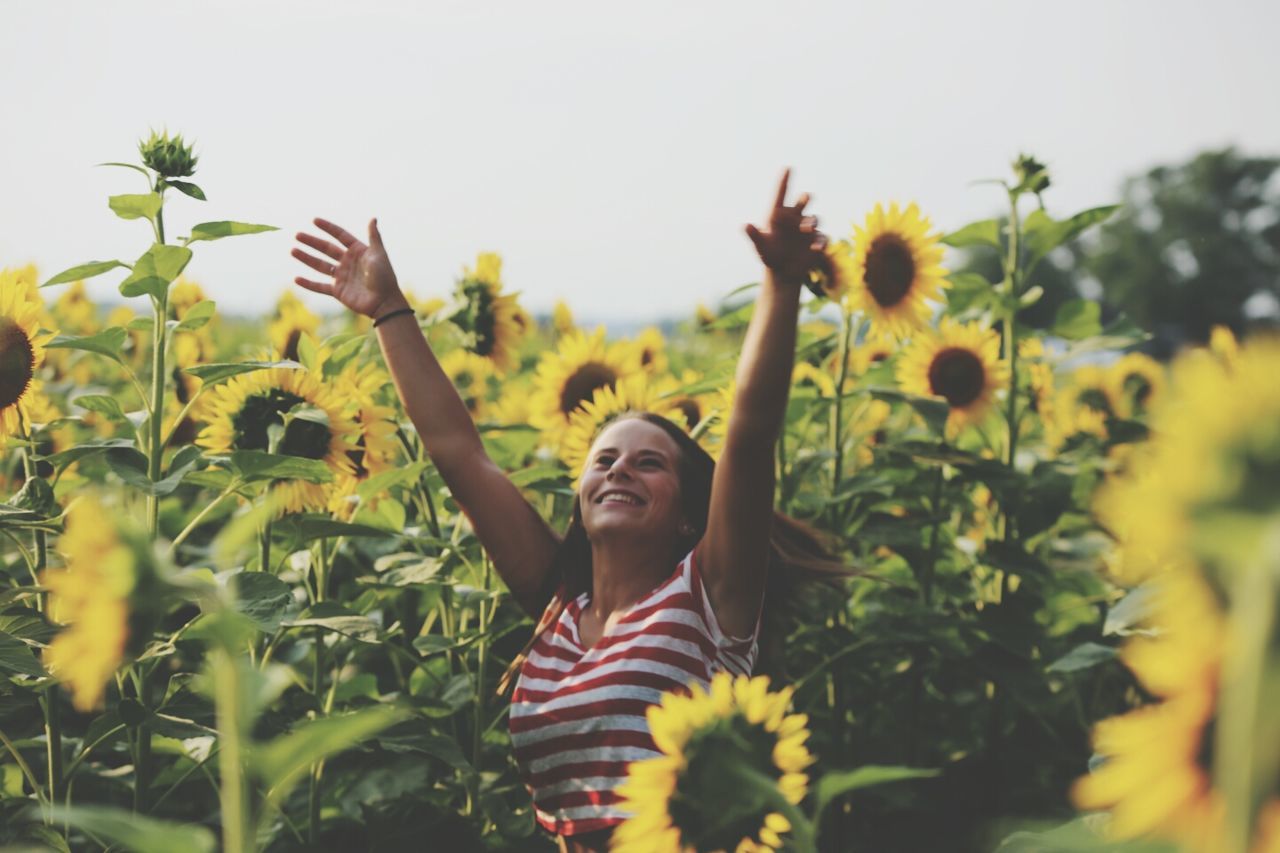 flower, growth, young adult, freshness, lifestyles, plant, beauty in nature, leisure activity, fragility, yellow, young women, nature, person, casual clothing, clear sky, sunflower, standing, field