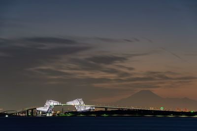 Illuminated bridge over bay against sky at sunset