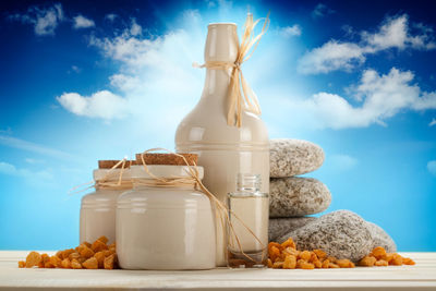 Jar and bottles on table against sky