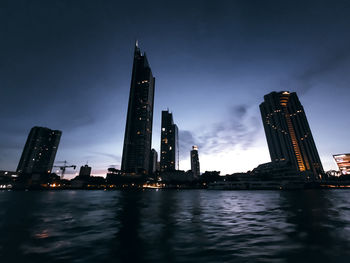 Illuminated modern buildings in city against sky at night