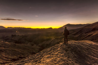 Silhouette man walking on landscape against sky during sunset