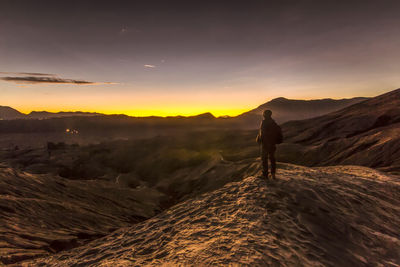 Man standing on landscape against sky during sunset