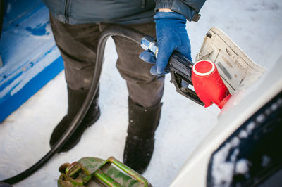 Low section of man refueling car with fuel pump during winter