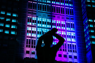 Silhouette man standing against illuminated buildings in city at night