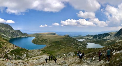 High angle view of people standing on field by lake against cloudy sky