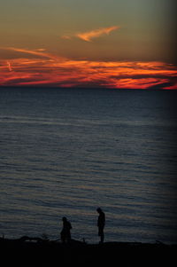 Silhouette people standing on beach against sky during sunset