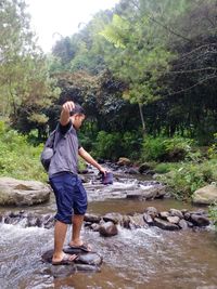 Full length of woman standing on rock in forest