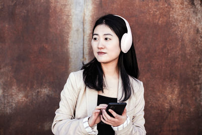 Confident business woman listening to music on headphones and mobile phone in city