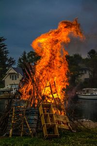 Bonfire in front of houses against sky at dusk