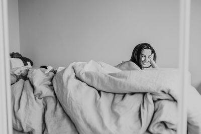 Portrait of smiling woman lying on bed against wall at home