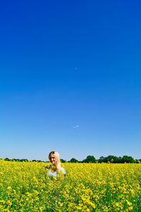 Portrait of smiling woman standing amidst oilseed plants on field against clear blue sky