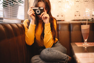 Teenage girl photographing with vintage camera while sitting in cafe