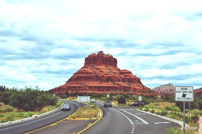 Road leading towards mountain against cloudy sky