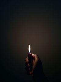 Close-up of hand holding lit candle in darkroom