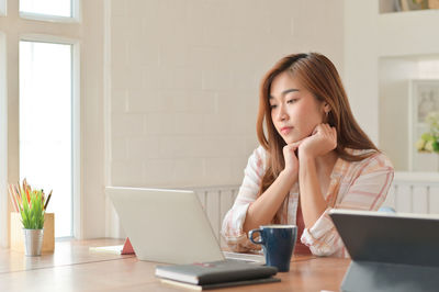 Young woman using phone while sitting on table