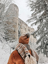 Rear view of young woman in winter clothes looking at castle ruins in winter, snow.