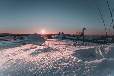 Snow covered field against sky during sunset