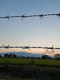 Barbed wire fence on field against sky during sunset