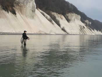 Side view of man fishing in lake against mountain