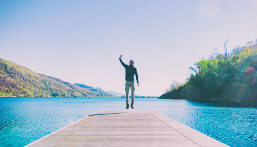 Rear view of man on pier over lake against clear sky