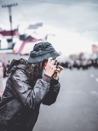 Side view of man standing against sky, holding camera