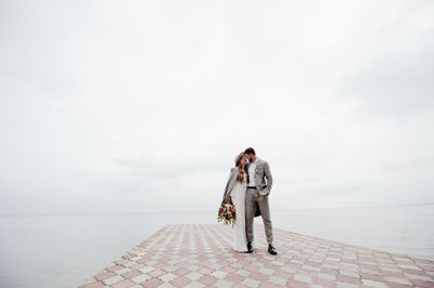 Bride and bridegroom standing on pier in sea during wedding ceremony