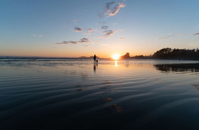 Silhouette people on sea against sky during sunset