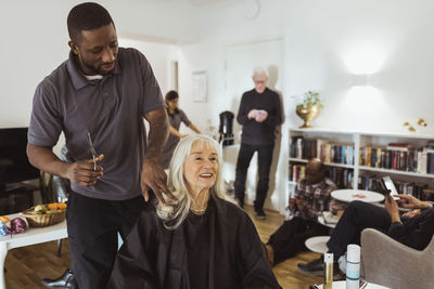 Male caregiver talking with senior woman while cutting hair in nursing home