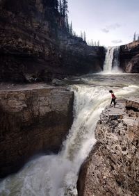 Scenic view of young woman looking down at waterfall