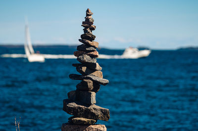 A closeup of a manmade pile of rocks against the blue sea with two boat sailing on the horizon.