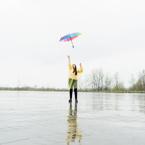 Beautiful brunette woman in yellow raincoat holding rainbow umbrella out in the rain