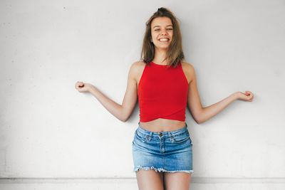 Portrait of a smiling young woman standing against wall