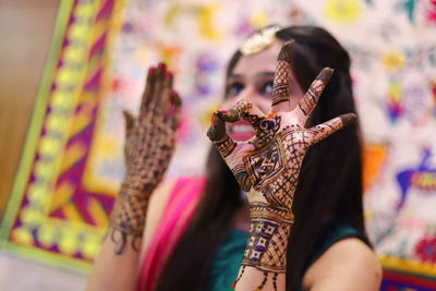 Woman with henna tattoo gesturing ok sign during wedding ceremony