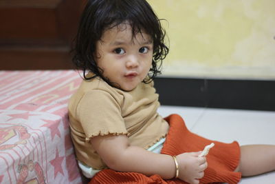 Portrait of cute girl sitting on bed at home